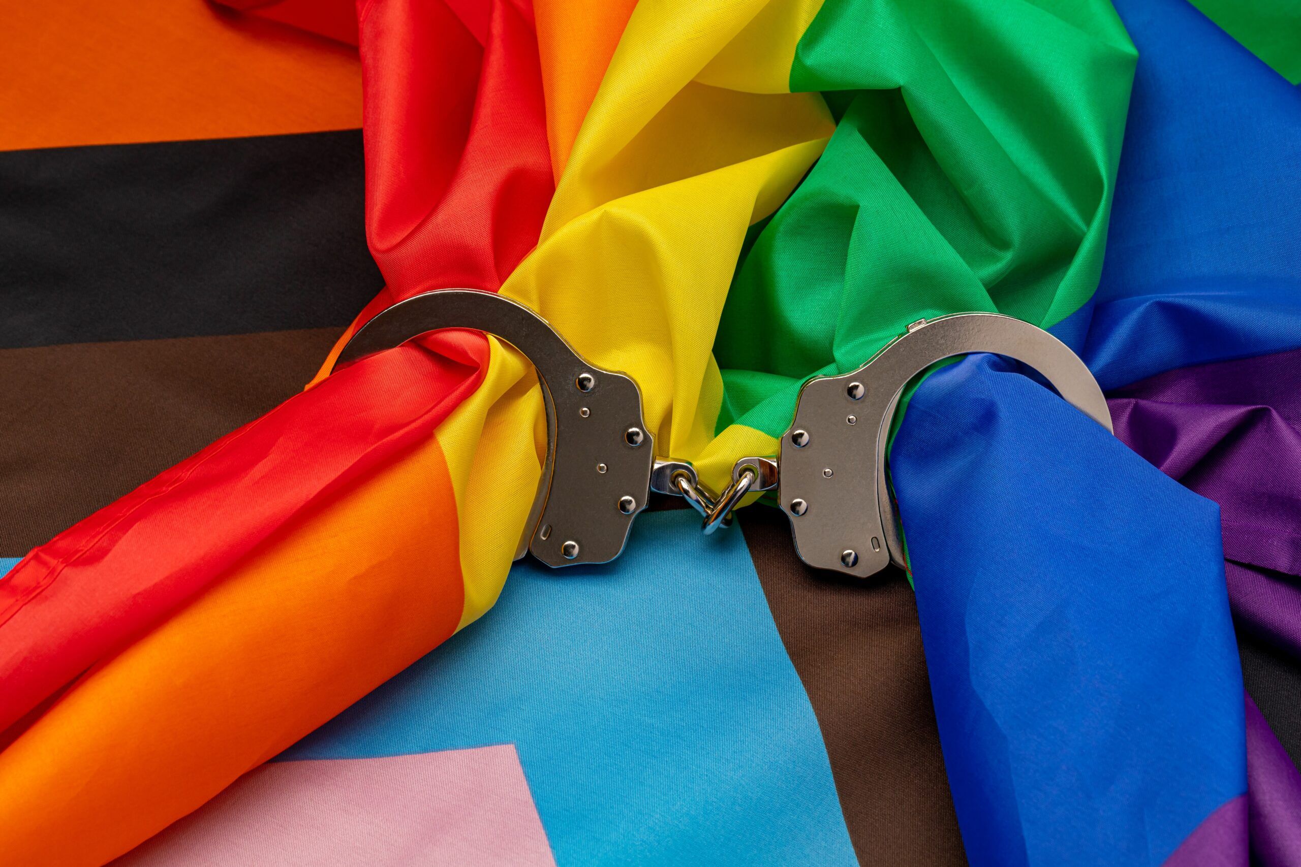 Rainbow pride flag and handcuffs. LGBTQ+ discrimination, legislation, and gay rights concept.