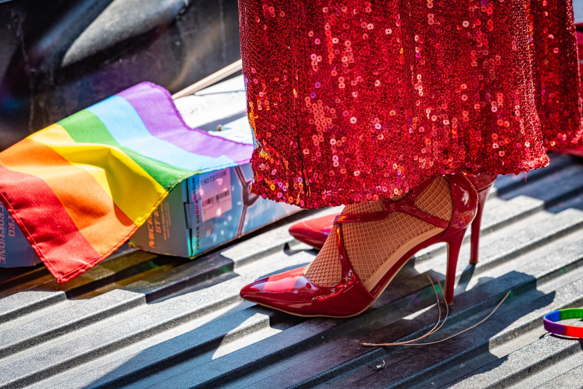 Photo of a queens red sequined dress, heels and a rainbow flag