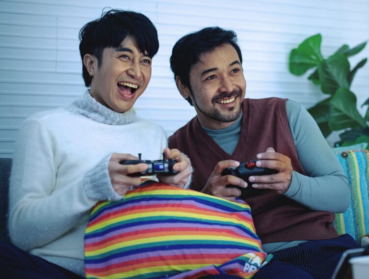 Male gay couple having fun playing video game console at home, LGBTQ family concept