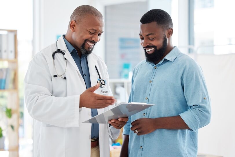 Healthcare, black man and doctor with clipboard, diagnosis and conversation for results, smile and care. Male patient, guy and medical professional with documents, paperwork for insurance and talking