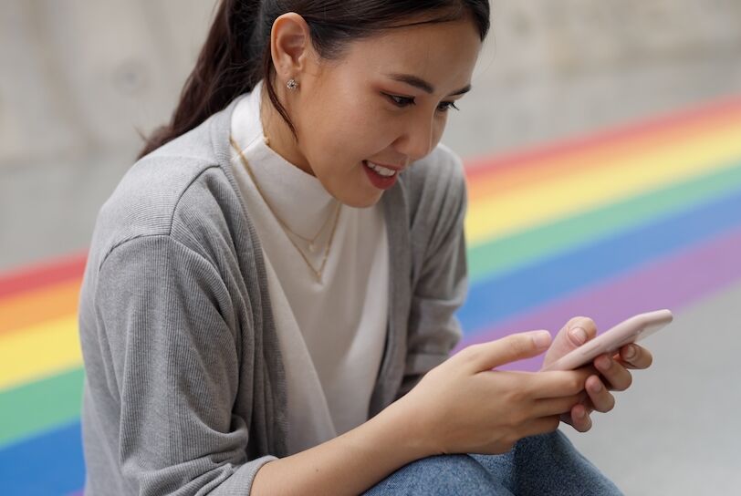 Young adult beauty queer asia gay people happy smile enjoy sit relax play social media app chat on phone at colorful rainbow color city street. Model teen girl student digital buying online shopping.