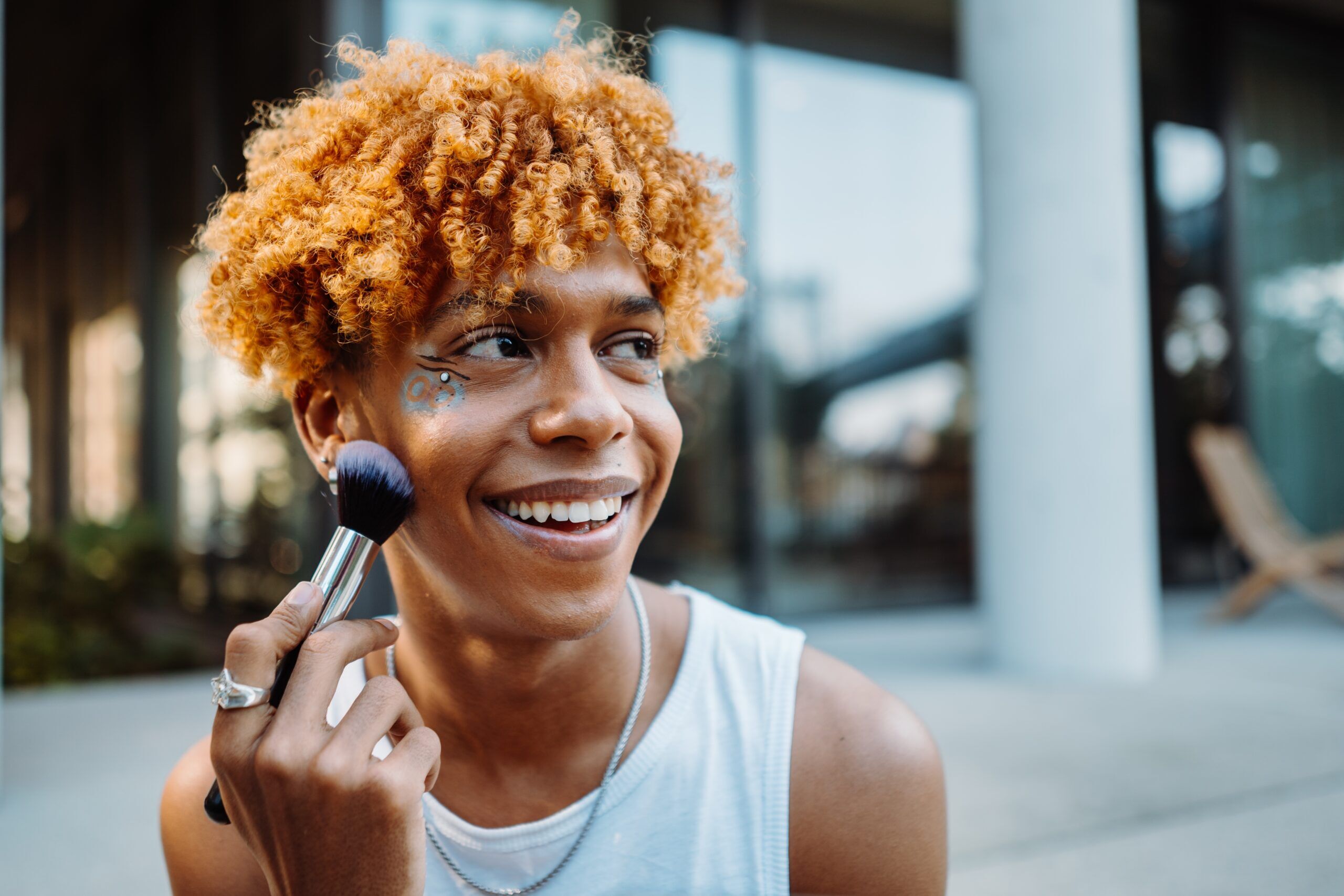 Positive multiracial charismatic boy preparing makeup at his face with visage brush