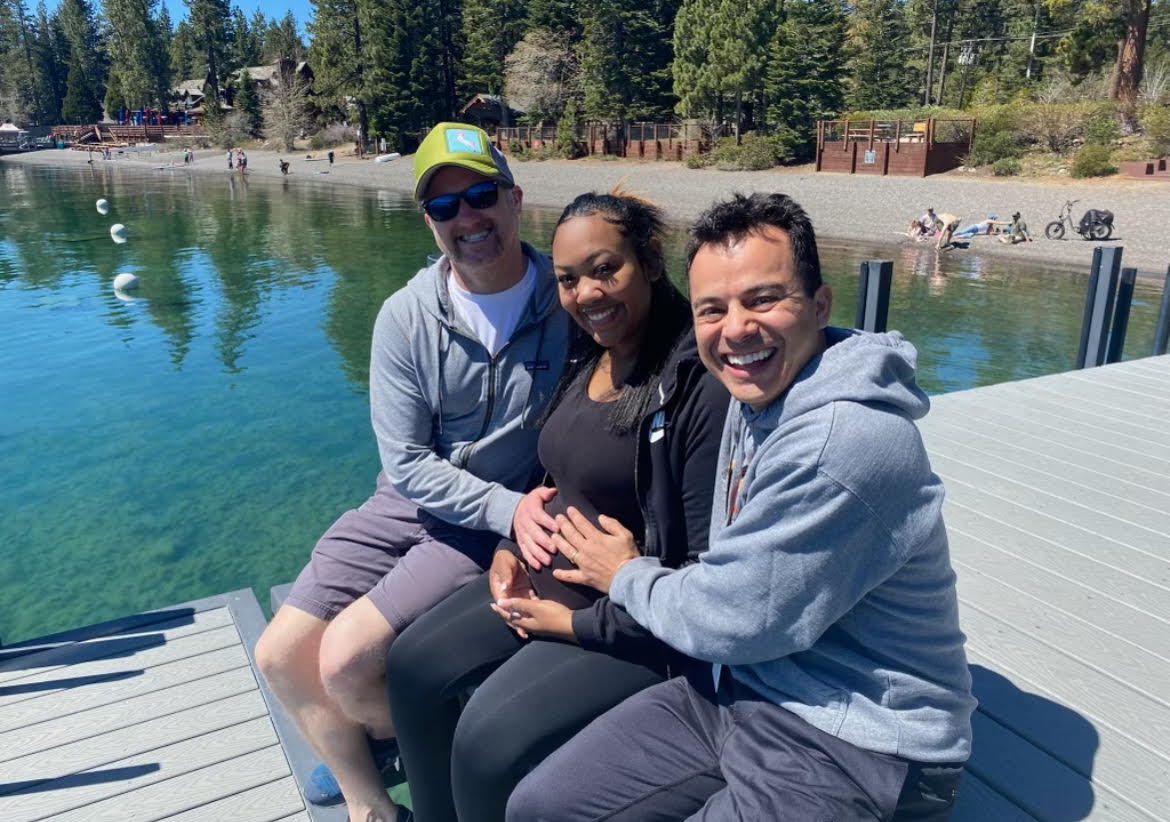 Pregnant Zarah Hilliard (center) with Randall Thomas (left) and Daryl Garcia (right) by a lake with their hands on her belly