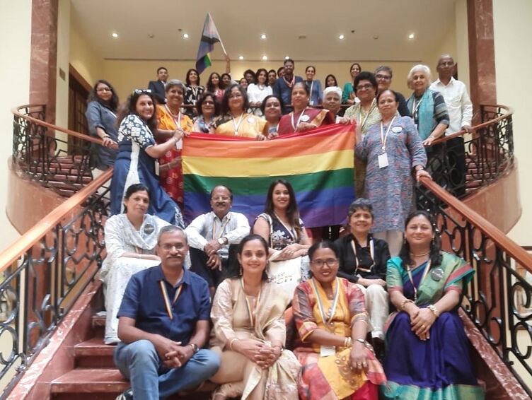 Sweekar members stand on a stairwell holding a Pride flag 