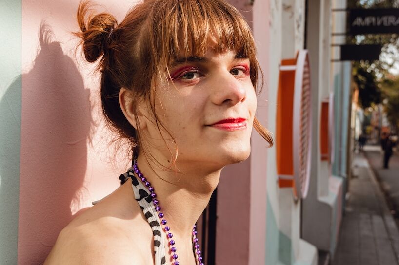 portrait of a young latin transgender woman smiling leaning against a wall in the street, looking at the camera halfway to the side, concept of inclusion with copy space.