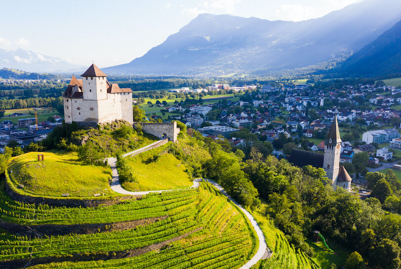 View from drone of stone Gutenberg Castle on top of green hill on background with small town of Balzers, Liechtenstein