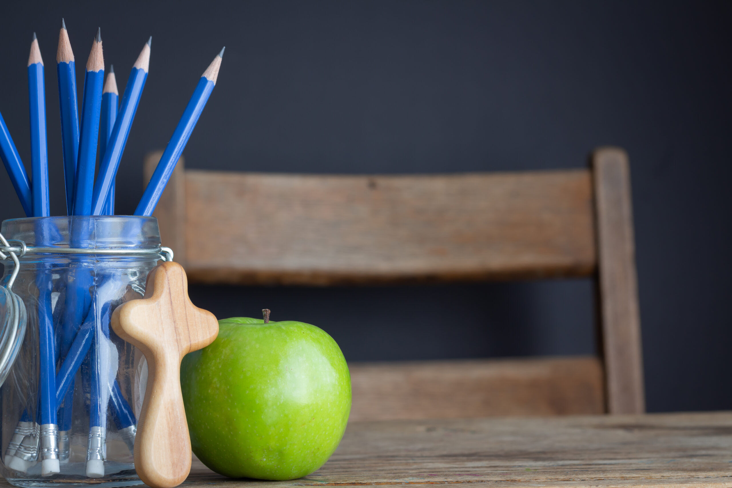 green apple, christian cross and jar of pencils on wood school desk with black background