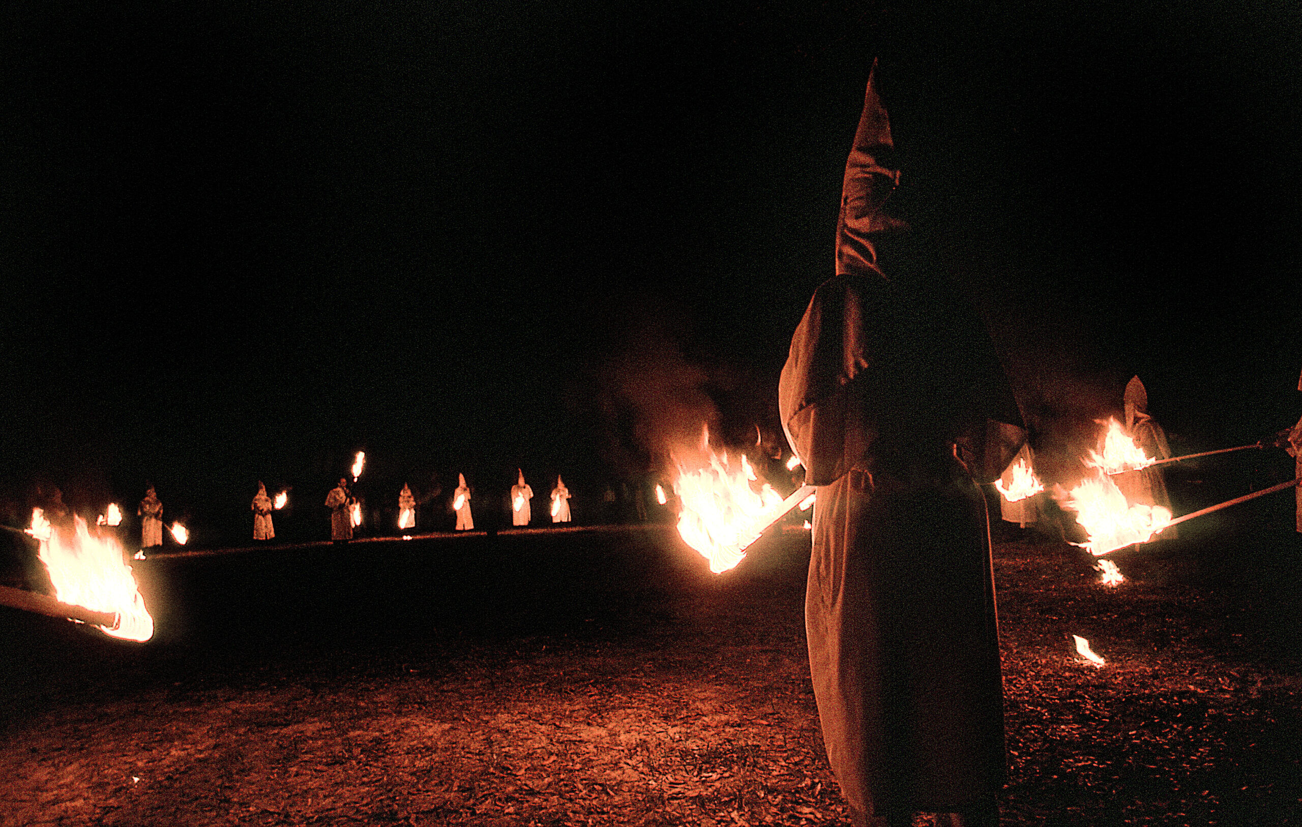 Panhandle, Florida, United States - circa 1995 - Ku Klux Klan KKK Night Ceremony, Members Wearing White Robes, Hoods and Carrying Burning Torches, Standing in a Circle