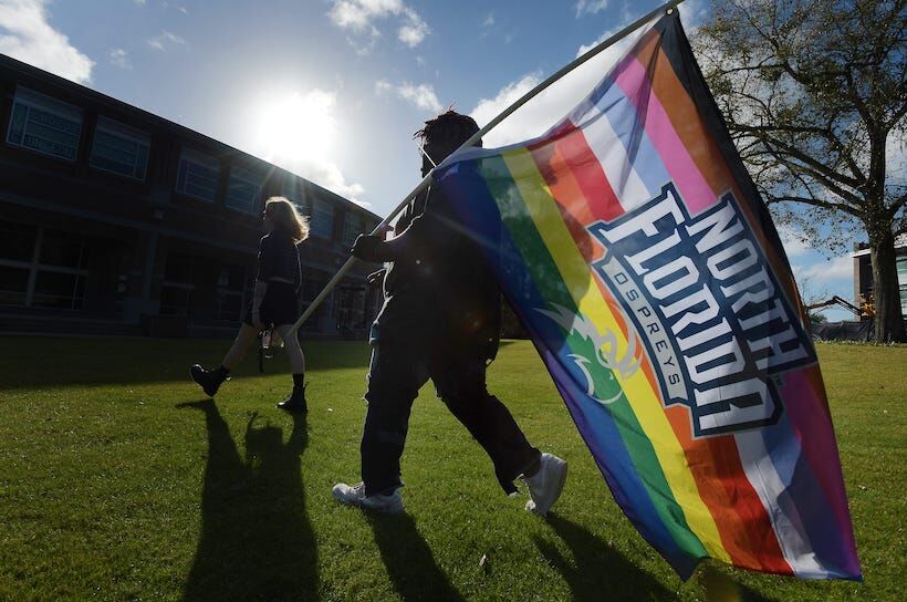 Sergio Sevieux carries an inclusivity flag with the UNF logo on it as he walks to join the rally on campus Wednesday afternoon. Around 100 students representing various sexual orientations rallied on the lawn in front of the University of North Florida's Fine Arts Center Wednesday, January 24, 2024 to protest the closure of the school's LGBTQ center to comply with state law which banns spending on diversity.