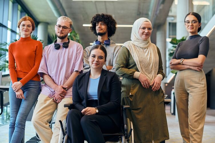 In a spacious and modern startup office, a diverse group of business colleagues, including a colleague in a wheelchair, collaborates and interacts, exemplifying inclusivity, diversity, and teamwork in