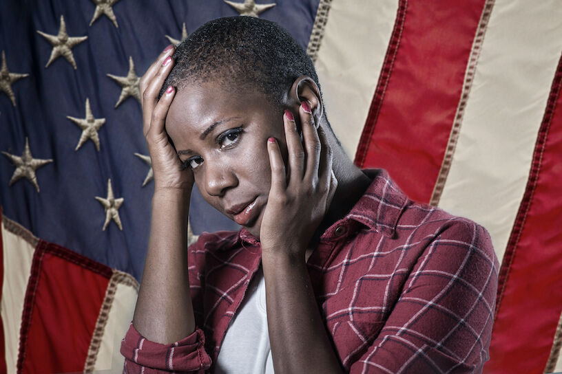 dramatic portrait of young sad and scared African American woman suffering racial discrimination and victim of abuse and racism feeling desperate and in pain in front of USA flag