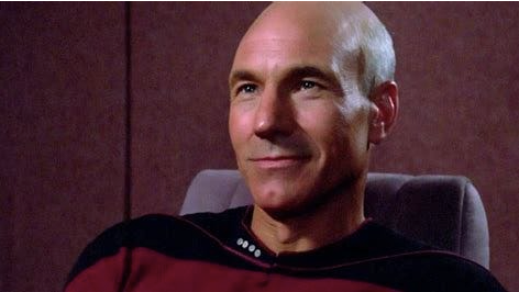 A bald white man in a Space Federation uniform sits in a chair aboard a spaceship