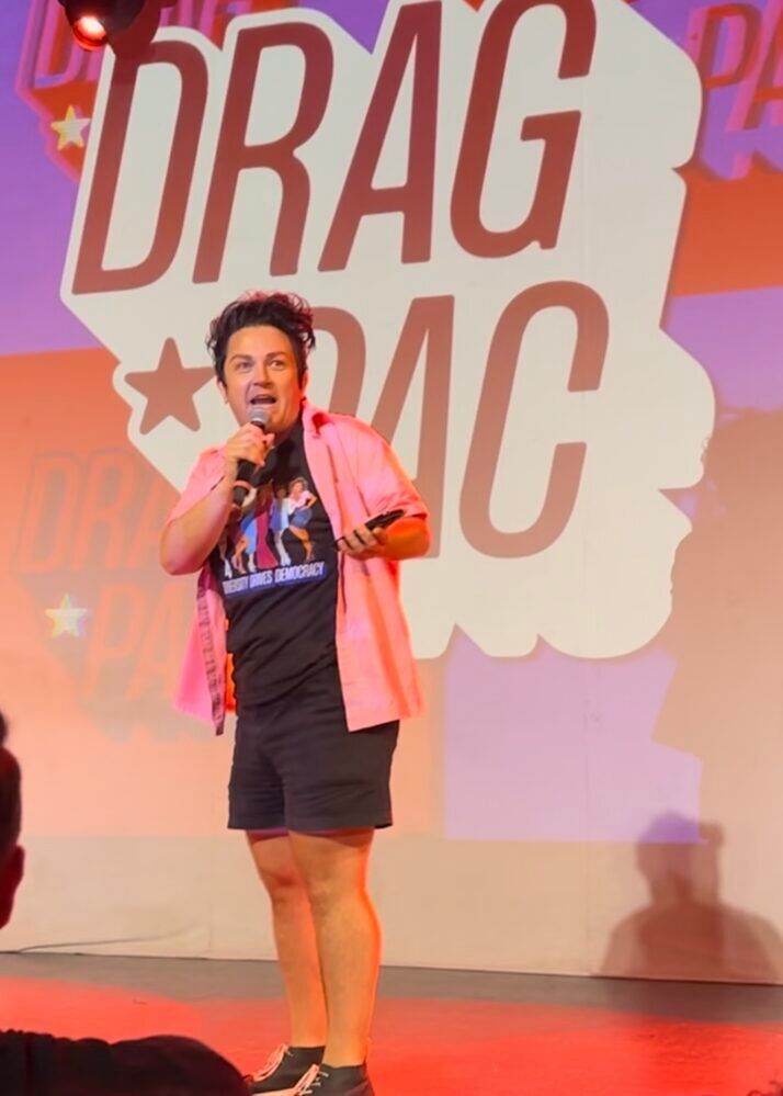 BenDeLaCreme standing on stage in front of a Drag PAC logo at Drag Night Chicago