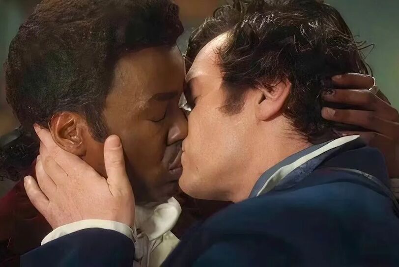 A black man and white man kiss, with their hands holding one another's faces.