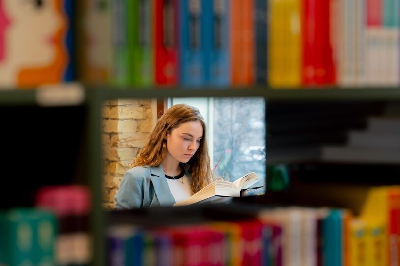 in bookstore near the window a beautiful student is sitting reading books preparing for exams