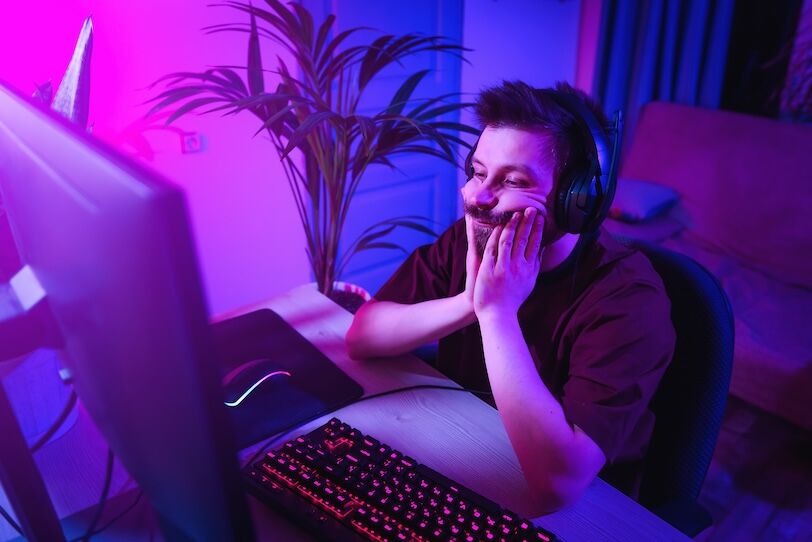 The man plays computer games at home. Young guy is bored during online learning. Neon light in the evening. Weekend at home at the screen.The boy lost, was tired and upset.