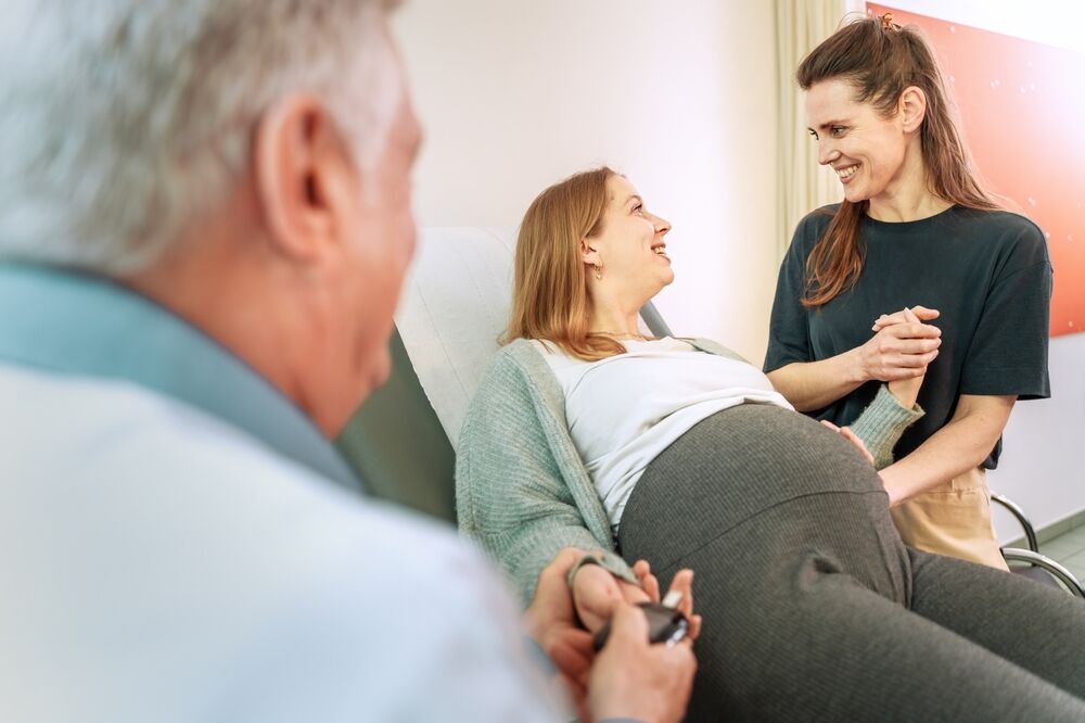 Two women and a doctor, one woman is pregnant