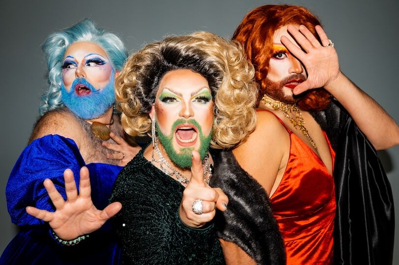 Group of drag queens in elegant outfits, standing together and striking poses of outrage, panic and confusion and ponting a finger at camera