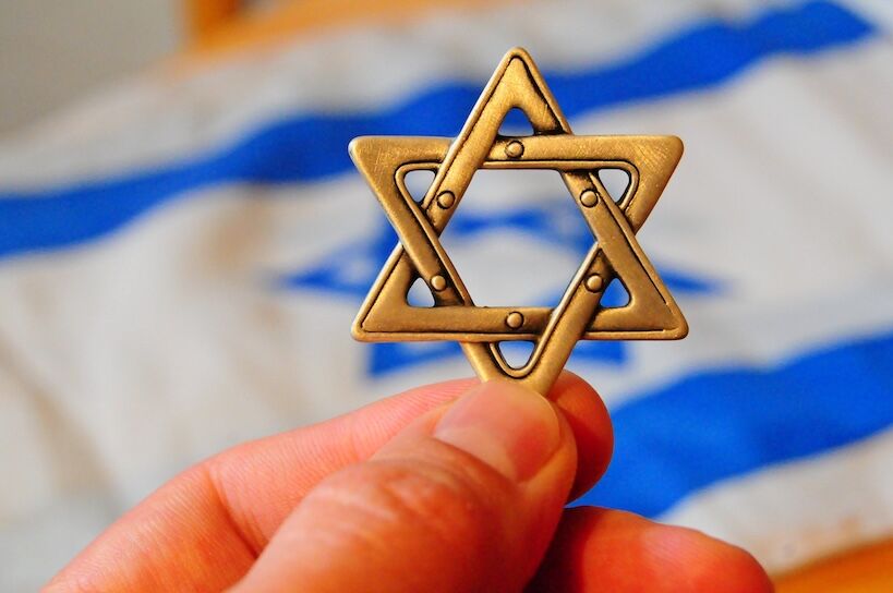 Fingers holding a Jewish star hexagram with Israeli flag on the background. Zionism, giyur, Judaism conversion concept. Israeli citizenship, Israel Independence Day, Yom Haatzmaut, Yom hazikaron.