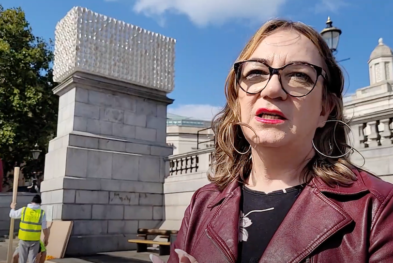 A trans woman stands next to "Mil Veces un Instante," a public artwork in London's Trafalgar Square.