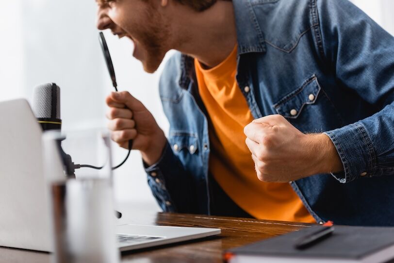 selective focus of angry broadcaster with clenched fist screaming in microphone at workplace