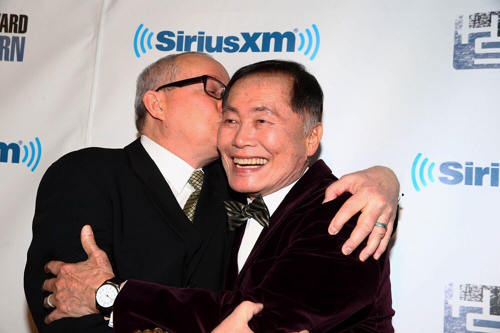 George Takei and his husband Brad Takei hug on the red carpet prior to the Howard Stern 60th Birthday Bash