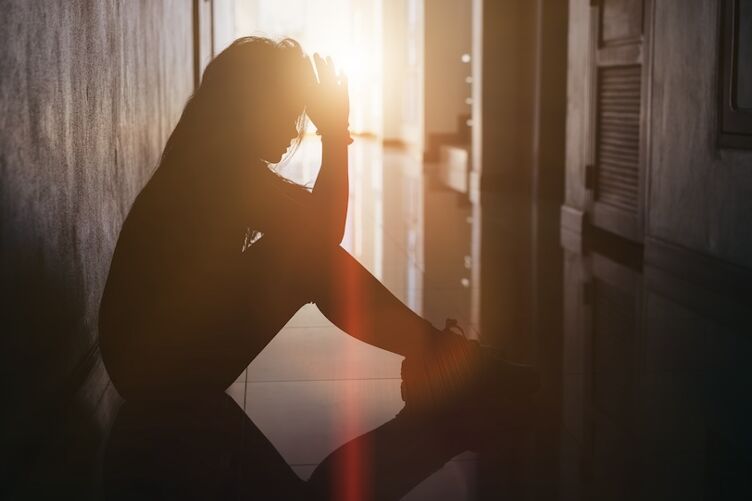 Silhouette of sad and depressed women sitting at walkway of condominium or office with backlit and lens flare,sad mood,feel tired, lonely and unhappy.