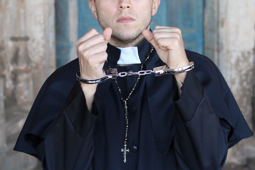 Handcuffed priest looking very upset