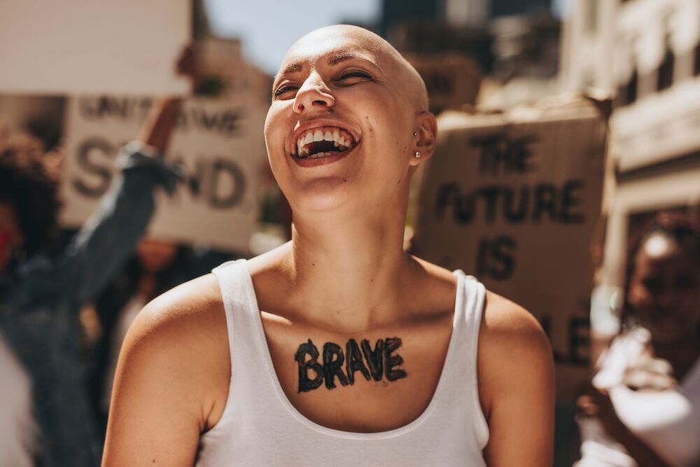 Bald woman laughing outdoors during a protest. Brave woman with group of protesters in background.