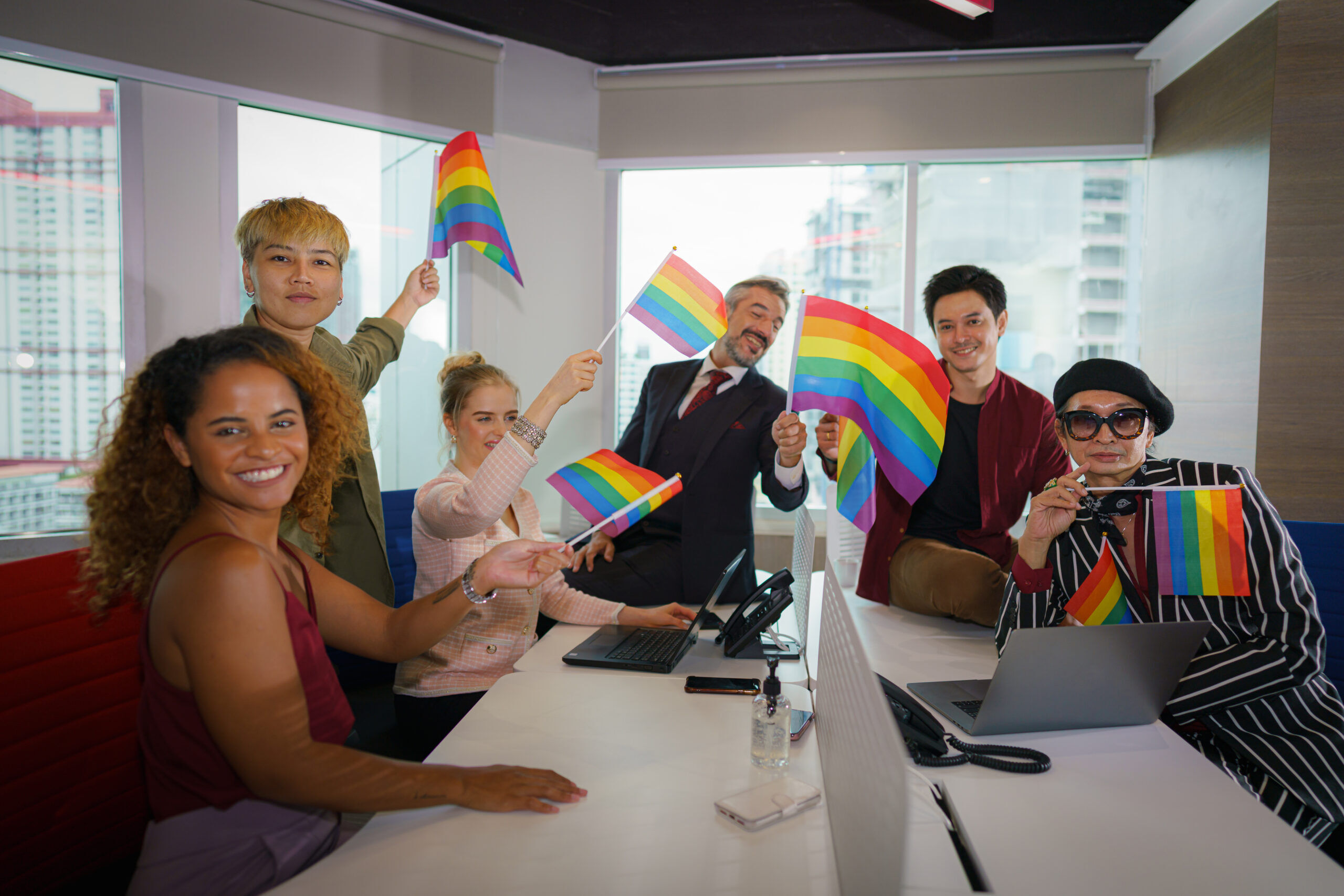 diverse business people (man, woman, gay, transgender, lesbian, asian, caucasian, african american, lgbtq) with rainbow flag on hand in business office working together as teamwork selective focused