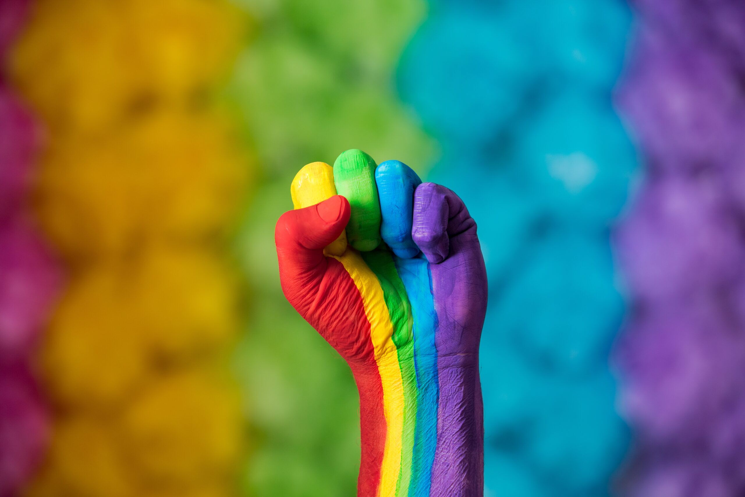 Rainbow colors painted hand raised making fist, sign. Rainbow colors background. LGBT pride symbol.