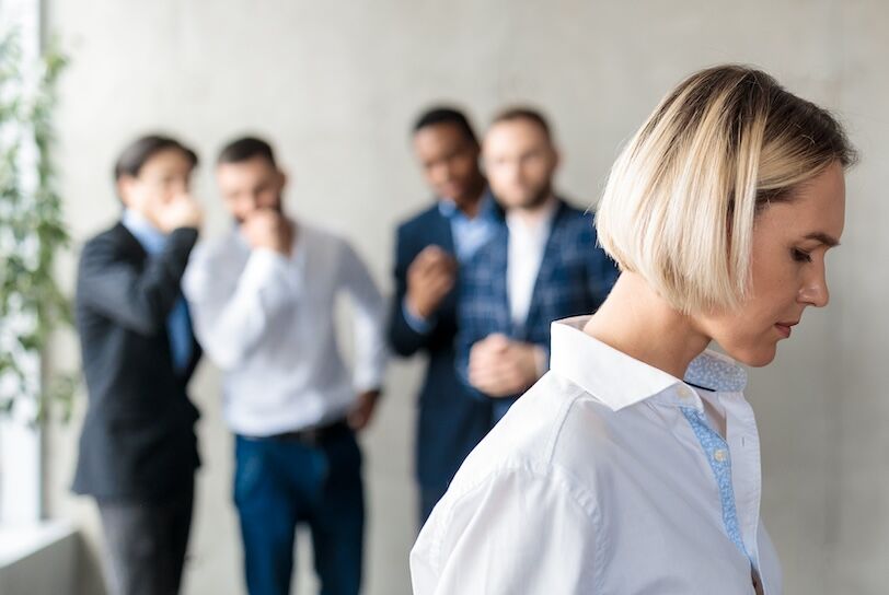 Workplace Bullying And Sexism. Male Colleagues Whispering Behind Back Of Unhappy Business Lady In Office. Victimization At Work. Female Discrimination Corporate Problem. Selective Focus, Panorama