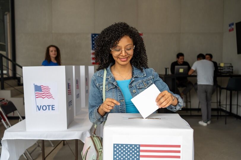 portrait of a young african american woman voting in the us election, placing vote ballot in the polling box, vote in America. Concept of choice, democracy and freedom