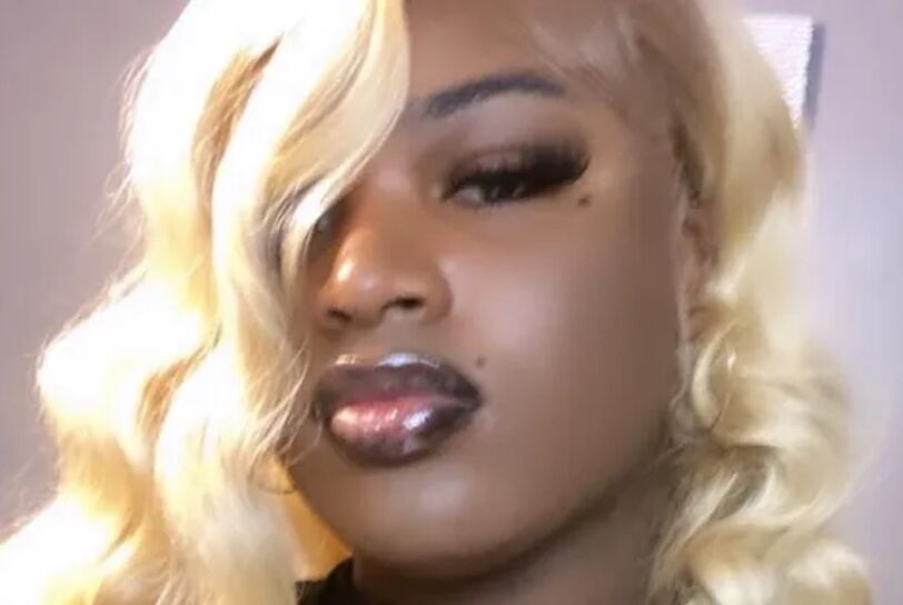 Cameron is a Black woman with red lipstick, drawn-on eyebrows and blonde wig