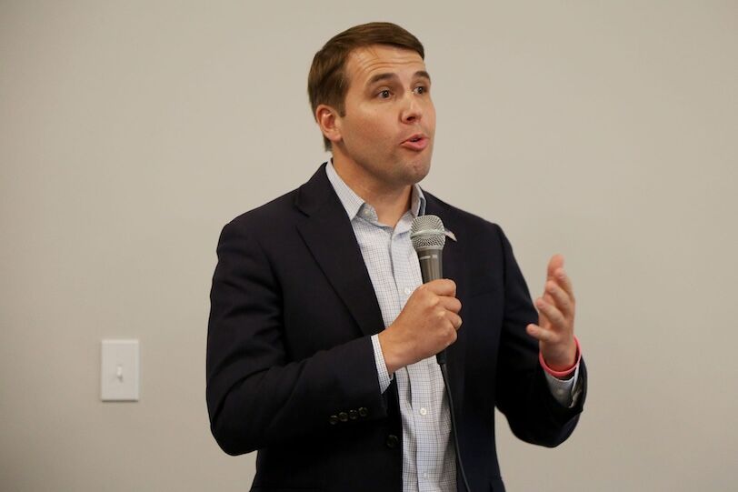 Pappas, a white guy with brown hair in his 40s, speaks into a microphone while wearing a blue blazer and white dress shirt open at the collar