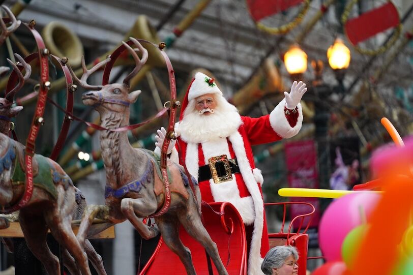 A man dressed up as Santa Claus waves to spectators during a holiday parade.