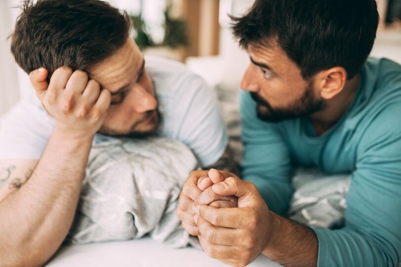 Gay couple lying in the bed, holding hands and working on their relationship. Mistakes are made, there is no reason to repeat them.