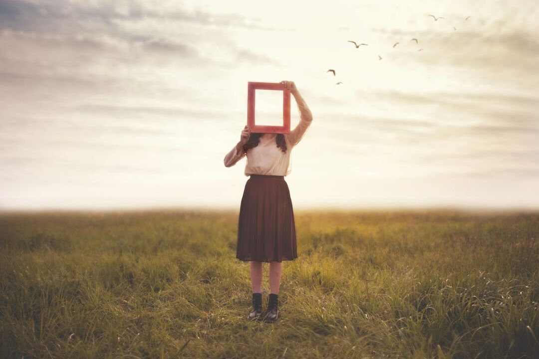 woman holds an empty frame that makes her face disappear reflecting the sky, abstract concept