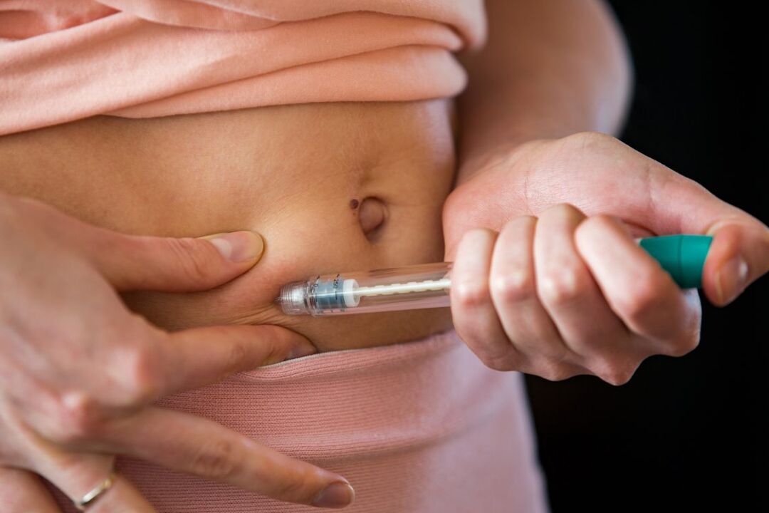 Person making hormonal therapy injection into their belly. Close up syringe pen. Person in bedroom, in vitro fertilization treatment