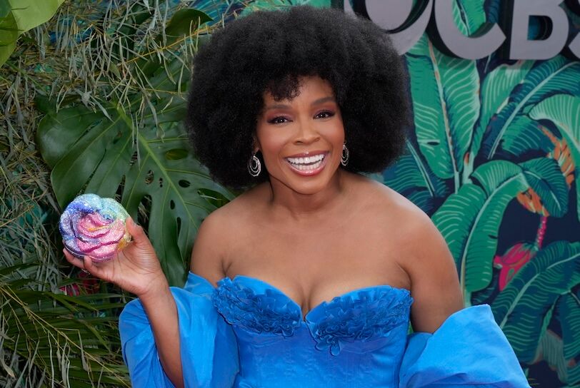 USATSI_20875113 Ruffin, a 46-year-old Black woman with an afro hairdo, wears a blue sleeveless dress and smiles while holding a flower whose petals are encrusted with rainbow sparkles. She stands against an artificial backdrop of green leaves.