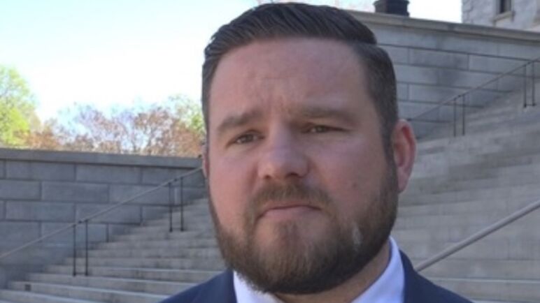 May is a fat white man with light brown facial hair and short hair. In this image, he wears a blue tie and suit while standing in front of the steps of a white stone building. May is a fat white man with light brown facial hair and short hair. In this image, he wears a blue tie and suit while standing in front of the steps of a white stone building.