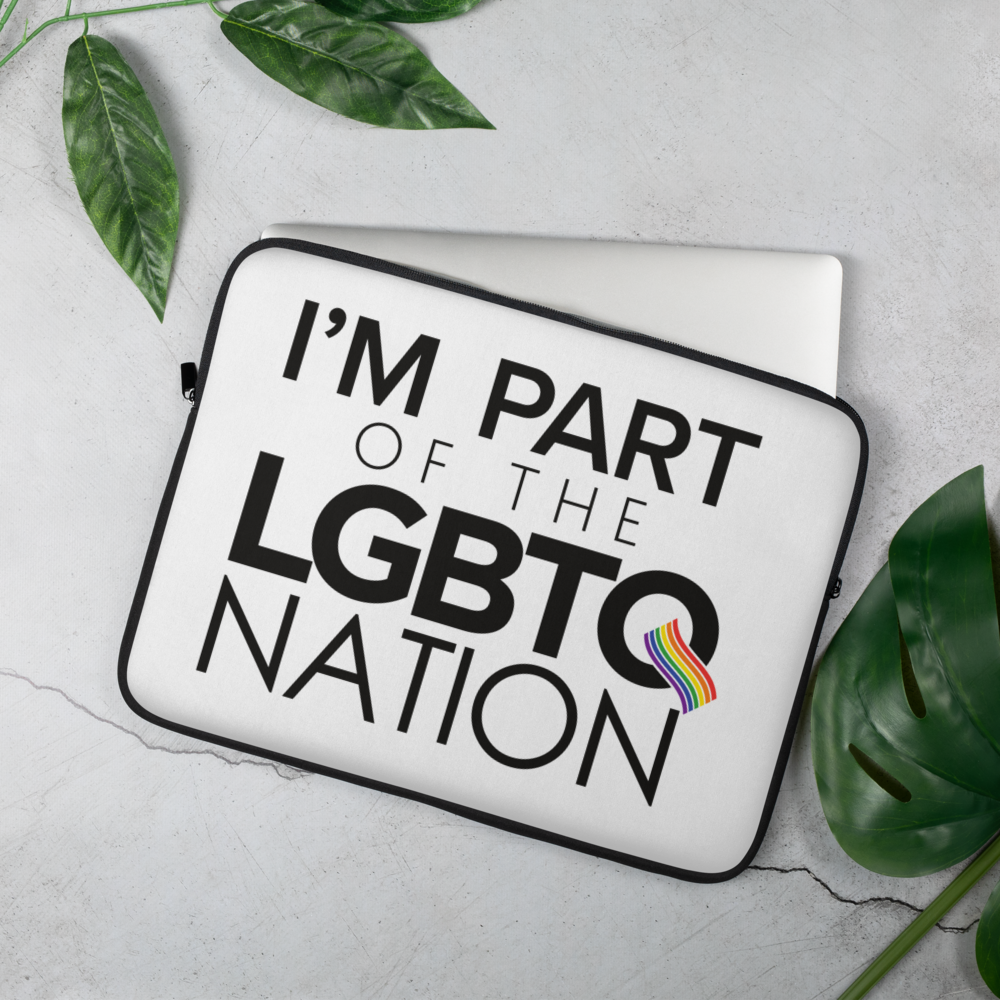 a laptop sleeve with big and bold “I’m Part of the LGBTQ Nation” phrasing on the front and a silver computer peeking out of the edge sits on a concrete slab with greenery around it