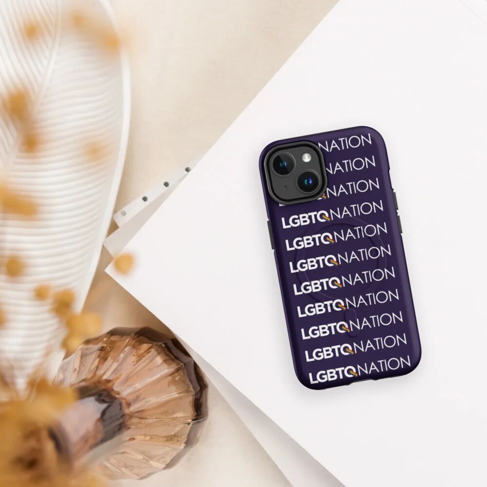 a deep purple phone case on an iphone with the LGBTQ Nation repeated vertically sits on a table with flowers blurred in the foreground